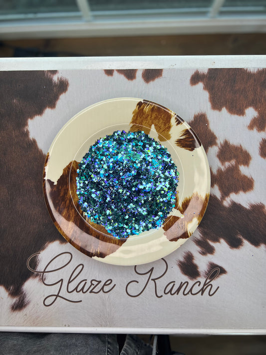 Decorative plate with blue glitter on a cow print background with 'Glaze Ranch' branding.
