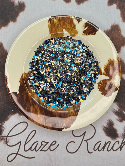 Decorative plate with blue and silver glitter on a cowhide-patterned surface with 'Glaze Ranch' branding.